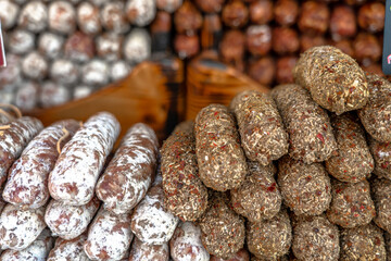 Stacks of dry-cured sausages - saucisson, typically made of pork, or a mixture of pork and other meats. Some variation contains spices and herbs, mushrooms, dried fruits, nuts, or cheese.