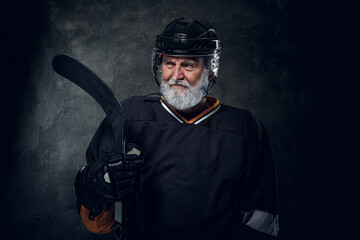 Studio shot of gray haired hockey player dressed in protective sportswear holding hockey stick.