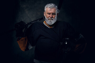 Studio shot of senior man professional hockey player with headwear and hockey stick.