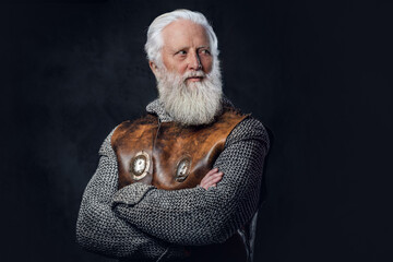 Shot of self confident elderly warrior dressed in antique armor with crossed arms against dark background.