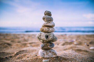 Beach stones stacked on top of the sand on a beach according to their size and the wavy sea in the background.