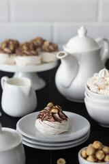 Close-up view of a meringue topped with chocolate drizzle and nuts, surrounded by ceramic tableware.