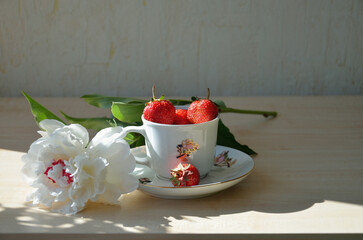 Still life, sweet fragrant strawberries in a porcelain cup with a white peony flower.