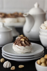 Dessert Pavlova with chocolate and hazelnuts. There is a dessert and white dishes on the table, a light background. Cream with mascarpone and whipped cream.