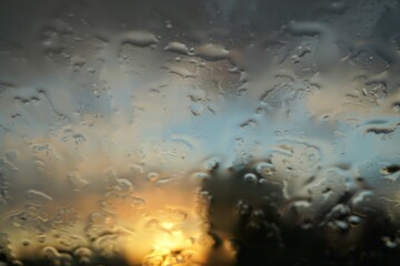Landschaft mit Sonnenuntergang und blauem Himmel hinter Glasscheibe mit Regentropfen bei Wind und Regen am Abend im Frühling 
