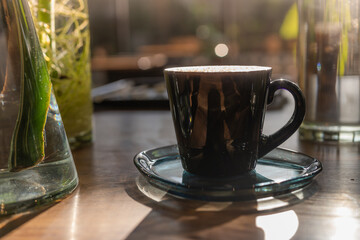 coffee latte art cup in coffee shop. hot Coffee in black mug on wooden table in cafe with plant in glass vase and sunlight background