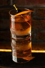 Crystal glass with bright cold alcoholic cocktail decorated with orange zest. Blurred background. Negroni cocktail.