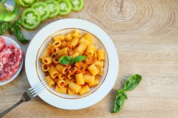 Pasta with green tomato sauce and Italian sausage on plate with wooden table background.Top view.Copy space