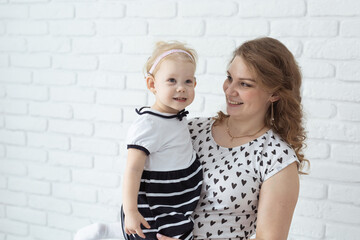 Mother holds her child with hearing aids and cochlear implants on white brick wall with copy space and place for advertising . Deaf and health concept