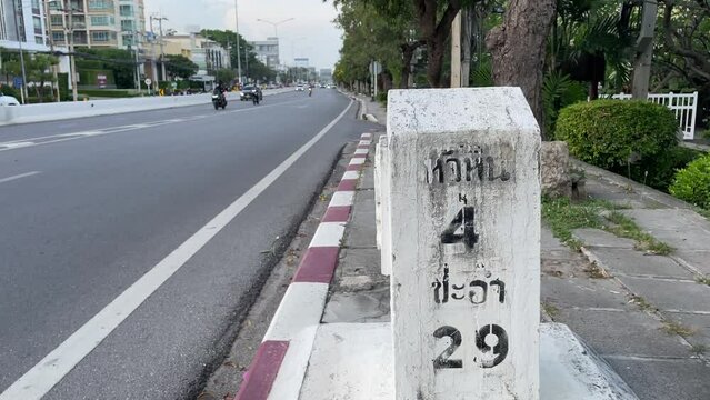 Traffic concrete distance road sign on road side ground with vehicles on road daytime. Display 4 kilometer to Hua Hin and 29 kilometer to Cha Am