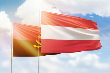 Sunny blue sky and flags of austria and angola