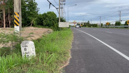 Suburban road side POV with vehicles on road daytime. Traffic concrete distance road sign display 8 kilometer to Hua Hin 