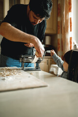 dad cooks homemade noodles with the kids, making tagliatelle with pasta machine on kitchen table
