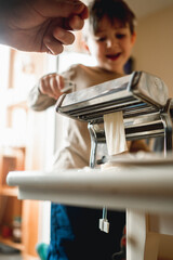 dad cooks homemade noodles with the kids, making tagliatelle with pasta machine on kitchen table