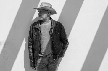 Portrait of adult man in cowboy hat against white wall on a sunny day