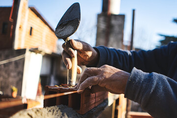Old man's hands gluing brick with trowel