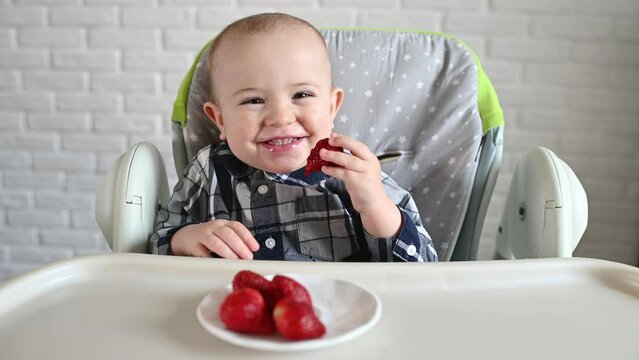 baby boy sitting on a baby highchair eating strawberries