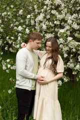 Fototapeta premium beautiful pregnant woman walks in a blooming garden. husband hugging pregnant wife