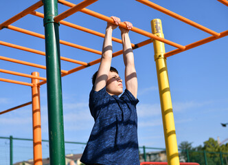 Fototapeta premium a teenage boy trains on a sports ground outdoors, he does physical exercises, a healthy lifestyle, a bright sunny day in summer