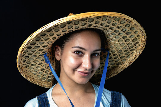 A beautiful young lady in an Asian hat smiles on a black background...