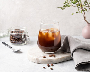 Iced coffee in a glass with ice cubes and grains on a light marble background. The concept of a cold summer drink