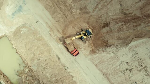 Aerial top down view of an excavator loading sand into a dump truck in sand quarry