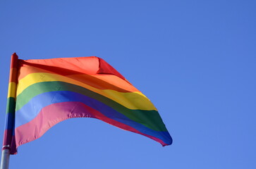 rainbow flag of an LGBT organization waving against a blue sky. Pride flag being waved in the breeze 