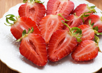 Ripe juicy strawberries cut in halves on a white plate.