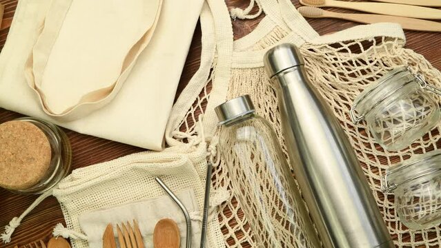 Zero waste eco friendly reusable objects such as reusable linen shopping bags, glass jars and wooden toothbrushes on wooden background, top view, rotating