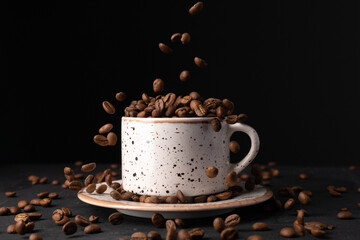 A cup with coffee beans in the air flying in flight like a spray. On black background, coffee shop advertising concept, copy space.