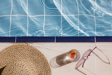 Straw hat, sunglasses and cocktail on swimming pool side. Blue sea surface with waves, texture...
