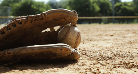 Sports equipment on field during summer shows ball and glove close up in dirt.