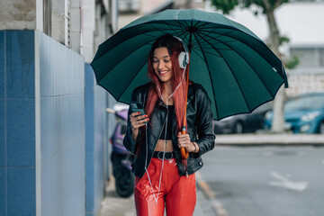 red-haired girl with mobile phone and headphones on the street with umbrella