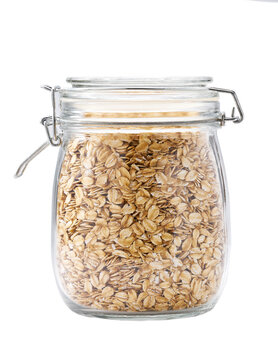 Heap of uncooked oatmeal flakes grains in glass storage jar isolated on white background.