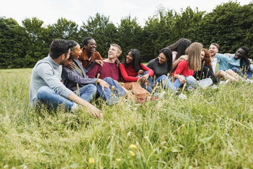 Multiracial happy people having fun sitting on grass outdoor - Focus on african girl with red shirt
