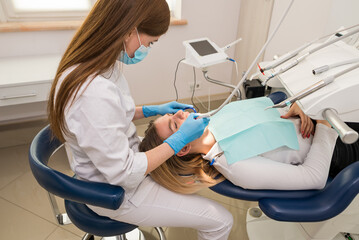 Fototapeta premium Dentist-hygienist conducts a teeth cleaning procedure for a girl in a dental clinic. Removal of tartar.