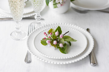Beautiful table decor for a wedding dinner with a spring blooming apple tree flowers. Celebration of a special event. Fancy white plates, wineglasses