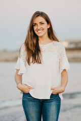 A young woman is smiling on a sandy beach near the water at twilight in Spain. A female tourist near the Balearic sea in Valencia.