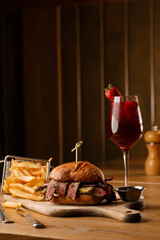 Pastrami sandwich on rye bread served with pickles and mustard sauce. Tasty sandwich with french fries potatoes and Sangria drink on dark background.