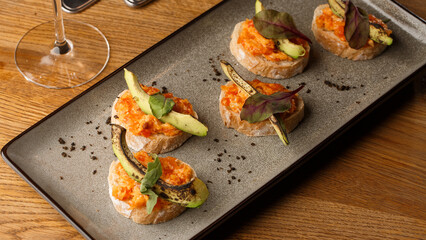 Fototapeta na wymiar baked bruschetta with salmon, cheese, sun-dried tomatoes and avocado in gray plate on bright background