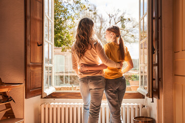 Teenage girl embracing with her mother while looking from the window