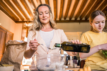 Concentrated woman pouring oil into the bowl while cooking at the kitchen with her teenage child