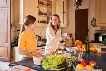 Woman standing at the table and chatting with her teen daughter while preparing dough