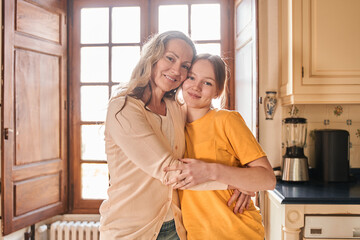 Mom holds her teen daughter to her heart while looking at the camera and posing