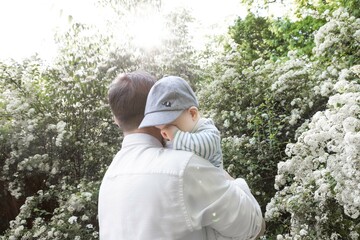 5 month old baby in a cap on his dad's shoulder against the backdrop of beautiful white flowers