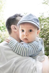 5 month old baby in a cap on his dad's shoulder against the backdrop of beautiful white flowers