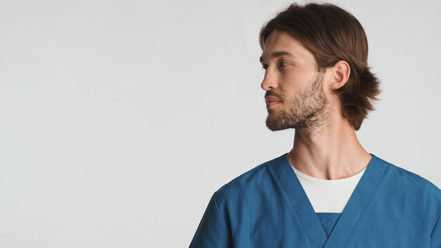 Young bearded male doctor looking on space for advertisement or promo over white background. Attractive intern in uniform