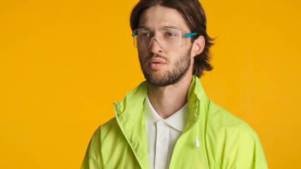 Portrait of guy wearing transparent protective glasses and acid jacket looking confident standing near space for advertisement or promotion against orange background