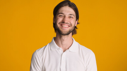 Young successful man sincerely smiling at camera against a colorful background. Cheerful male model posing in studio. Happy face