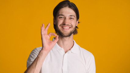 Glad man showing okay gesture approval sign giving positive reply against orange background. Attractive guy asserting everything is ok over colorful background